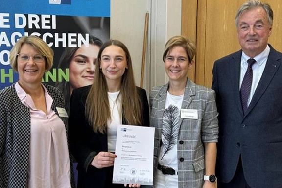Alina Kleinle bekommt Urkunde und steht neben Simone Heidenreich und zwei Vertretern der IHK