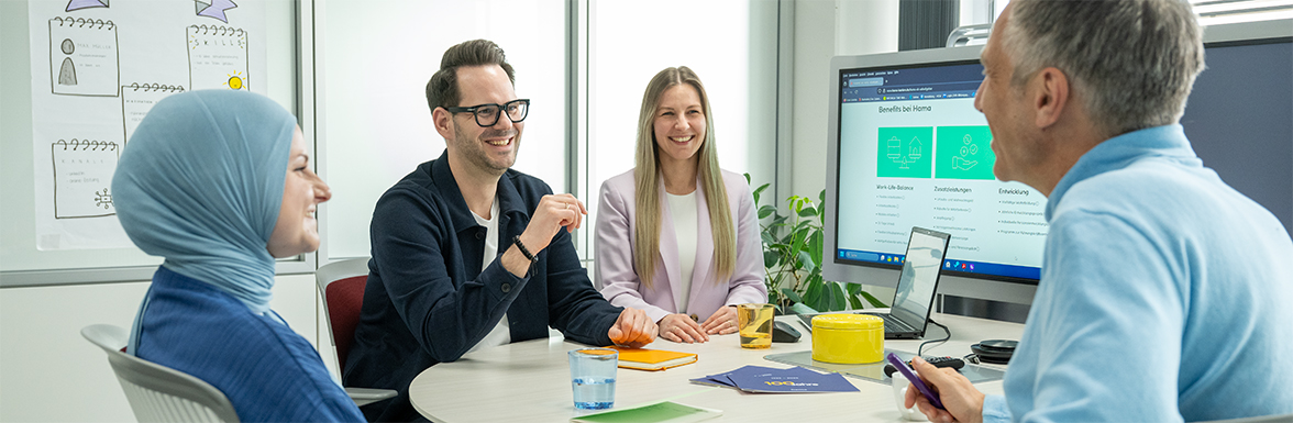 Drei Kollegen in einem Büro. Eine Frau betritt mit Dokumenten, der Mann trägt einen Rucksack, die zweite Frau hält Laptop und Headset.