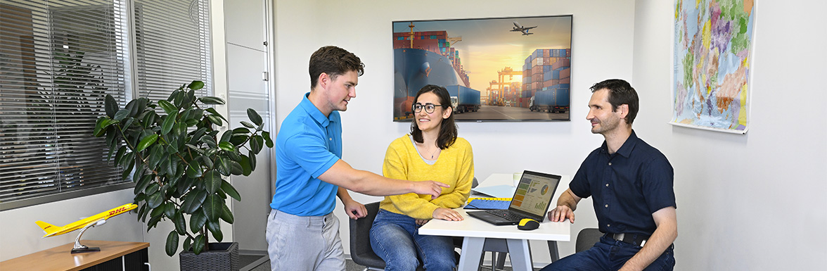 Drei Kollegen sitzen und stehen an einem Stehtisch im Büro zusammen.